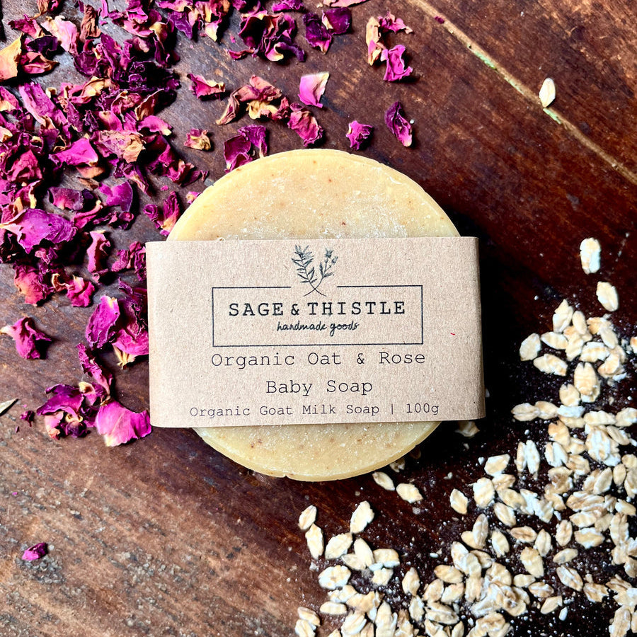 Organic oat and rose baby soap bar with a label on a wooden surface with dried rose petals and seeds.