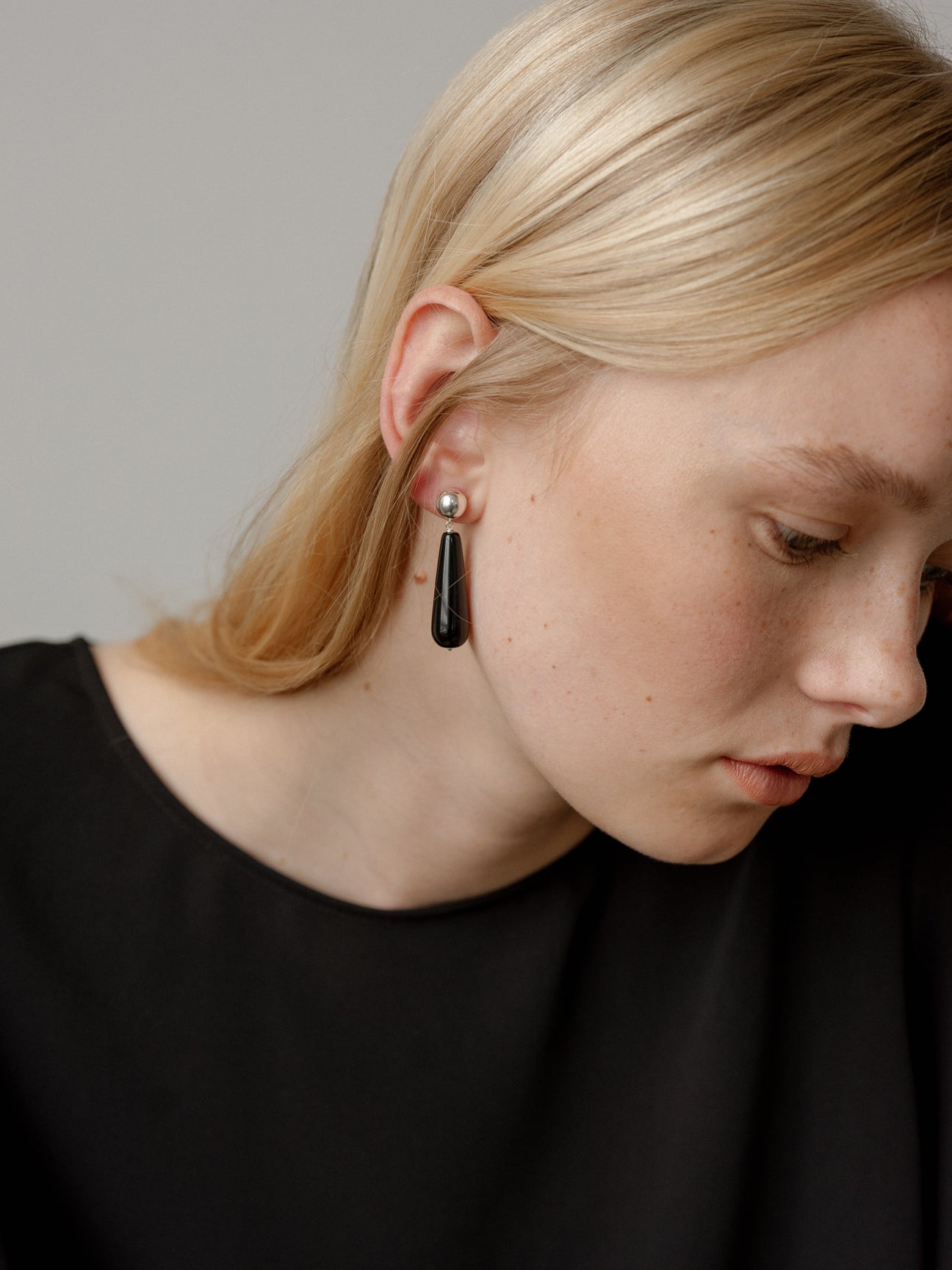 Close-up of a person wearing a black earring against a neutral background