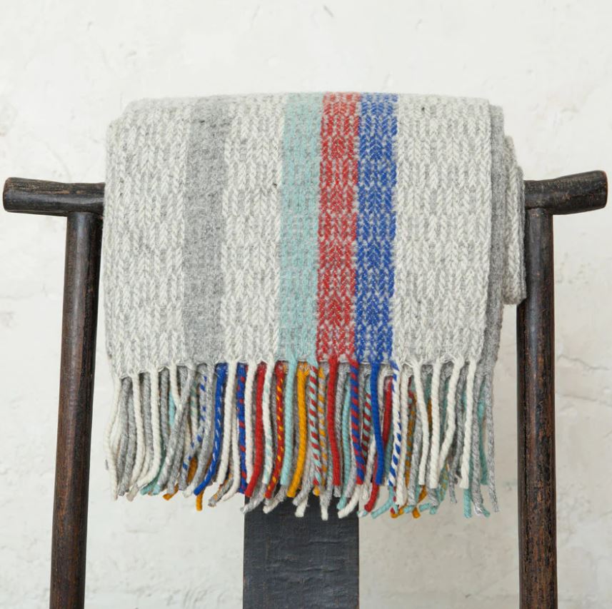 Textured blanket with colorful fringe draped over a wooden chair against a white wall.