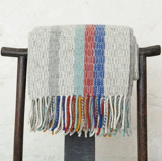 Textured blanket with colorful fringe draped over a wooden chair against a white wall.